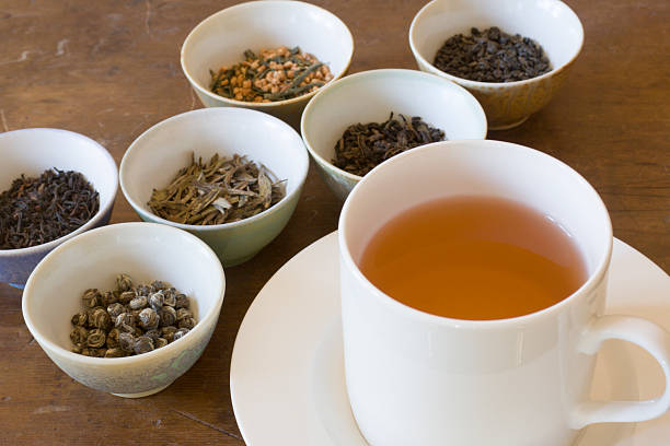 Hot Tea in Cup Near Leaf Varieties for Tasting Selections Selection of dried tea leaves from around the world and a cup of hot brewed tea, ready for comparative tasting and sipping. The white saucer holds a full pour of the beverage. Chinese, Japanese, and Indian varieties such as oolong, jasmine, darjeeling, and other black and green choices are shown. sri lankan culture stock pictures, royalty-free photos & images