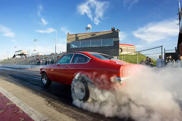A bright red race car peels out on the starting line of a raceway's drag strip.