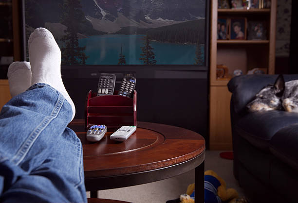 Couch Potato Man sits and relaxes while watching TV at Home.... remote control on table stock pictures, royalty-free photos & images