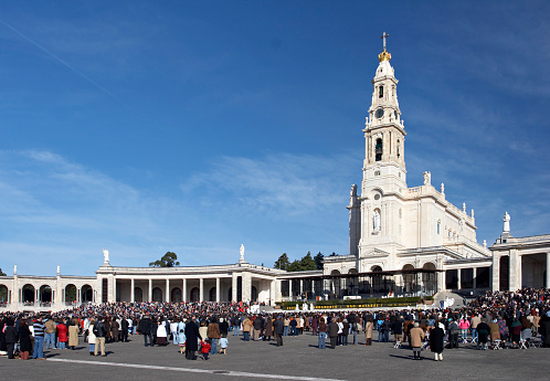 An image of a religious event at a church in Fatima, Portugal.  A large crowd of people surrounds the elegant white church, which features a tall chapel.