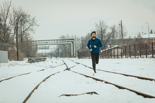 An active young man is running and doing exercises across the old railroad during the winter training outside.