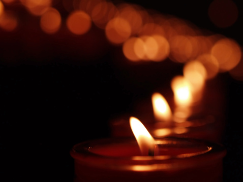Candles in a row with shallow depth of field, with light glow of other candles in the background