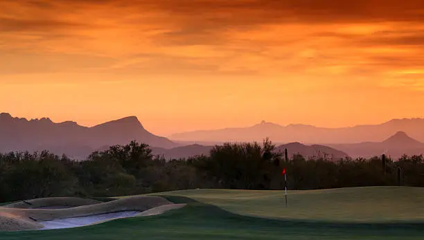 An amazing desert golf hole with sunset. Golf course scenic in Tucson, Arizona, United States. A beautiful golf green and fairway with the desert and mountains in the background. Arizona is one of the most popular golf destinations in America. Millions of snowbirds and seniors head to the region for winter every year. 