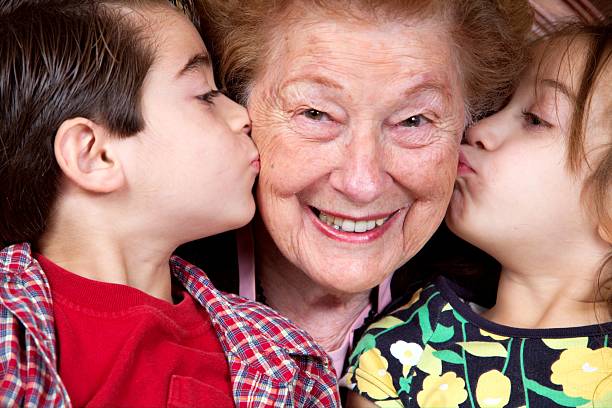 Two grandkids lovingly kissing their happy grandma stock photo