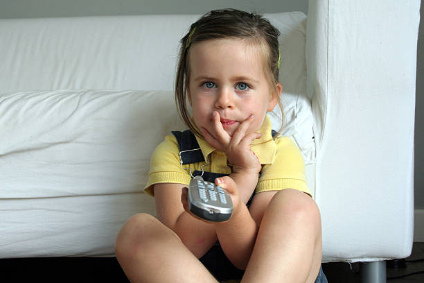 Young girl holding remote and watching television stock photo