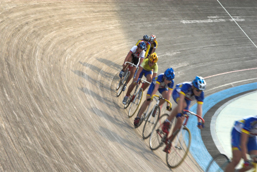 A group of cyclists speeding up in a velodrome. Motion blur.
