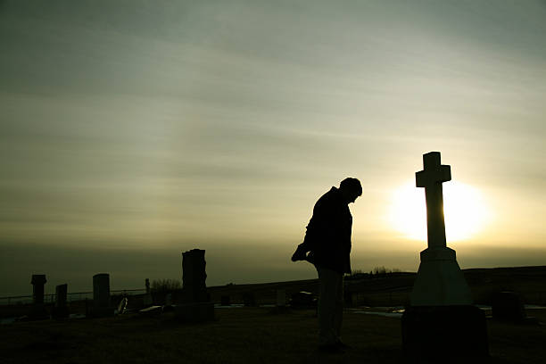 Silhouette of Caucasian Man Mourning at Graveyard A man remembers a loved one beside a tombstone at a graveyard. Additional themes include death, loss, funeral, remembering, tribute, memorial, memorial day, veteran's day, sadness, heaven, cemetery, and grief. Unrecognizable man in 30s.  soldier grave stock pictures, royalty-free photos & images