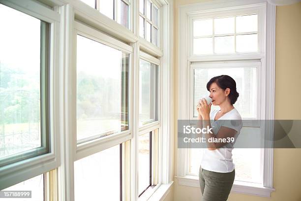 Woman Standing By A Window Drinking Coffee Stock Photo - Download Image Now - Adult, Adults Only, Coffee - Drink