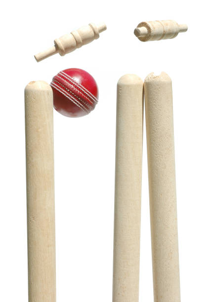 A white cricket ball striking orange electronic cricket wickets with dislodging bails and illuminating LED lights on a night sky background - 3D render