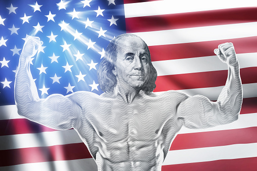Muscular Benjamin Franklin showing double biceps against American flag on background. Compositing of real photos.