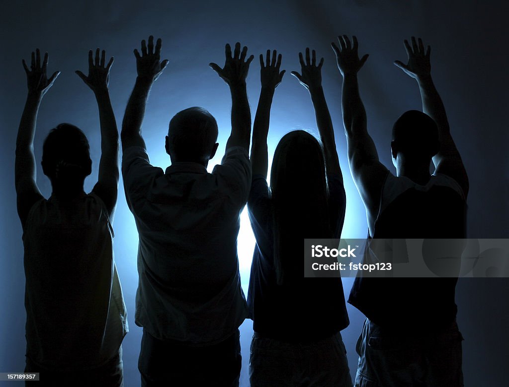 Group of people silhouette. Arms raised in praise. Blue light. Four people offering praise or worship.   Spirituality. Blue light background.  Cult, religion, followers. Silhouette. Cult Stock Photo