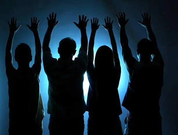 Four people offering praise or worship.   Spirituality. Blue light background.  Cult, religion, followers. Silhouette.