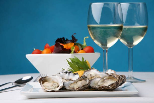 Fresh delicious opened oysters in ice and two glasses of champagne are on a black stone textured background. Delicacies at a restaurant. Healthy sea food. Side view. Close-up shot.