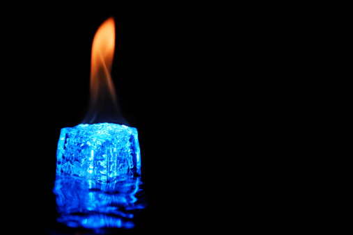 Photo of cool blue ice cube burning against a black background.