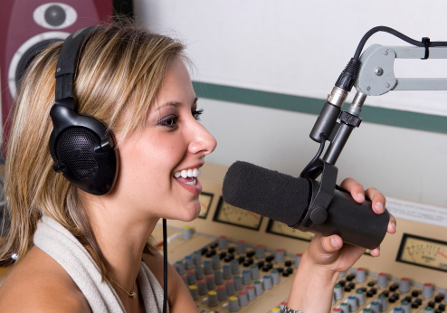 A beautiful, blonde, female DJ is working hard at the radio station.