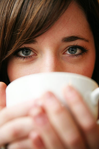 Brown hair, green eyed woman hiding behind a coffee mug stock photo