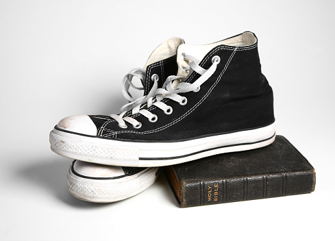 An old fashioned pair of tennis shoes sitting on an antique bible against a white background.