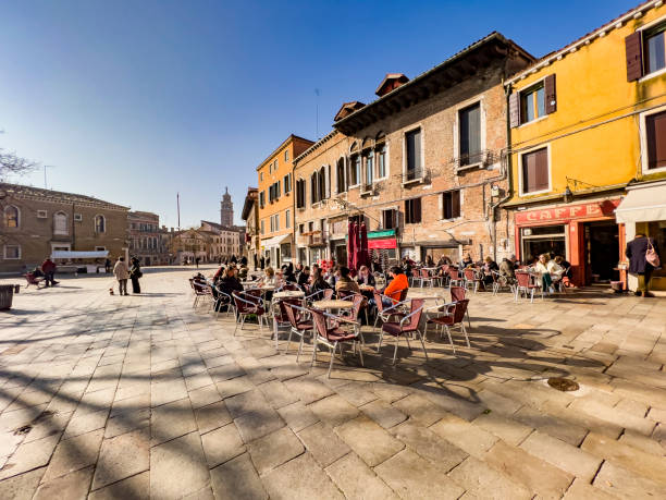 Venice, Italy, 01/31/2023; people walking and sitting in a beautiful cafe outside at a local town square on a cold sunny winter day, enjoying the sun and the togetherness with friends and family.