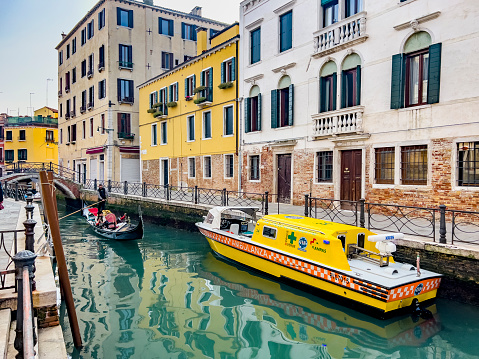 Venice, Italy, 02/01/2023; A yellow water ambulance boat mooring in a narrow canal in Venice, Italy. The three Italian words on the ambulance say 
