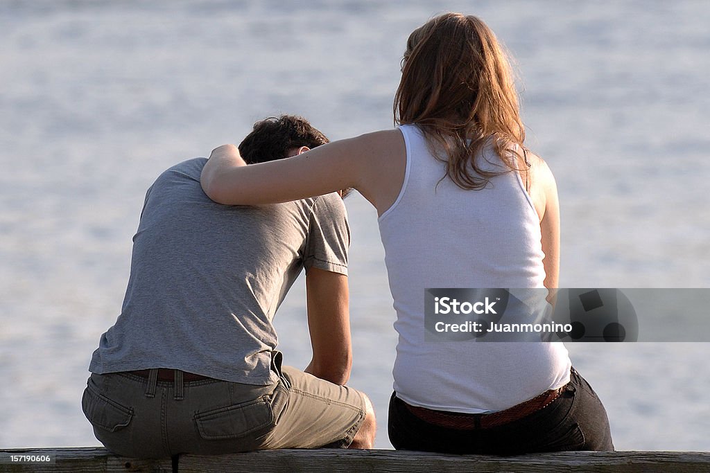 concerned woman comforts frustrated man at a beach Woman with her concerned boyfriend Consoling Stock Photo