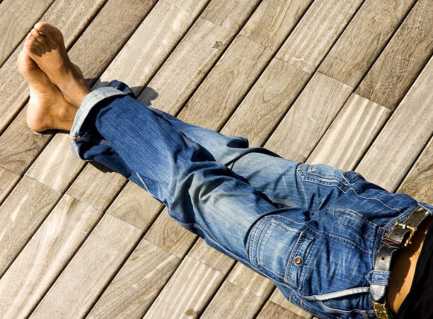 A photograph of some legs in jeans with ankles crossed Blue jeans clad legs of male in total relaxation effortless deck denim jeans stock pictures, royalty-free photos & images