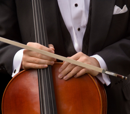Close-up of a cellist holding a cello and bow. The musician is dressed in a tuxedo, prepared for a classical concert. The musical instrument held by his two hands.