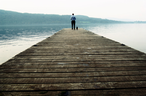 businessman standing at the end of a wooden jetty on a deserted misty lake.