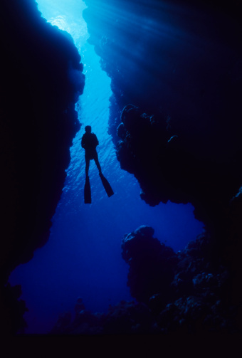 Silhouette of scuba diver in opening of sunny cave. Solomon Islands
