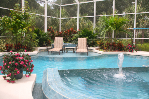 Swimming pool with fountain, flowers, chaise longue, tropical foliage and palm trees. Florida luxury living. Summer vacation. 