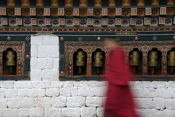 Prayer wheels with monk Bhutanese prayer wheels with young monk passing by buddhist prayer wheel stock pictures, royalty-free photos & images