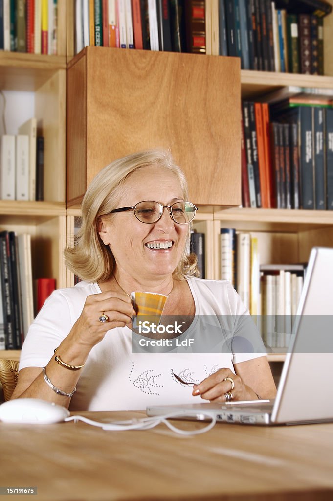 Donna anziana con computer portatile e libri su sfondo scaffali - Foto stock royalty-free di 60-64 anni