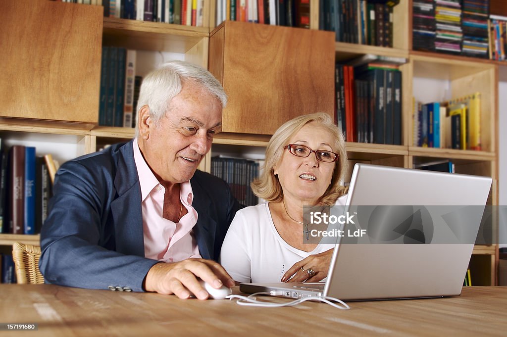 Dos Senior con ordenador portátil y libros estantes en el fondo - Foto de stock de Pareja mayor libre de derechos