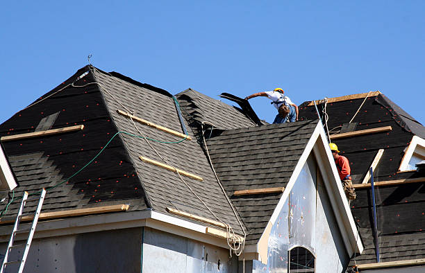 Roof Workers on top of house with blue sky Construction workers putting shingles on the roof of a house.  installing stock pictures, royalty-free photos & images