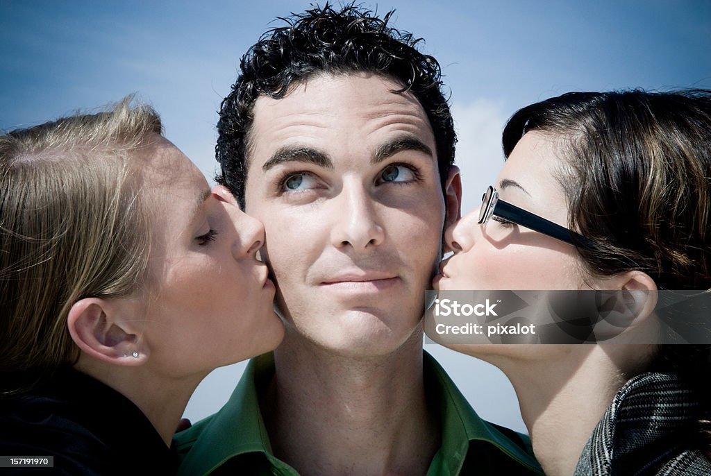 Lucky Man II Attractive gentleman simling and looking up, being kissed on his cheeks by two beautiful girls. blue sky in the background. Human Sexual Behavior Stock Photo