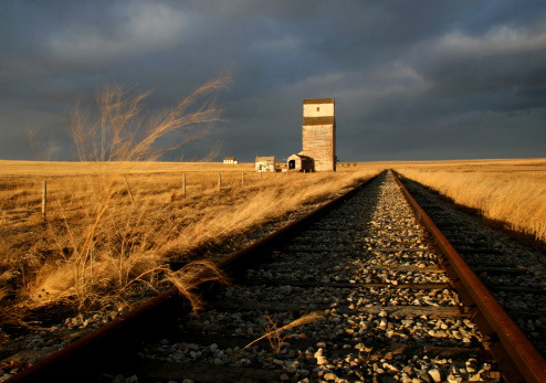 An abandoned grain elevator on the prairies. Rural scenic in southern Alberta, Canada. The railway was a key component of settling the western plains. Now many lines are abandoned and used no more. Wooden grain elevators were also a key part of farming and agriculture in the early days. The wooden grain elevators have now been replaced by concrete structures. 