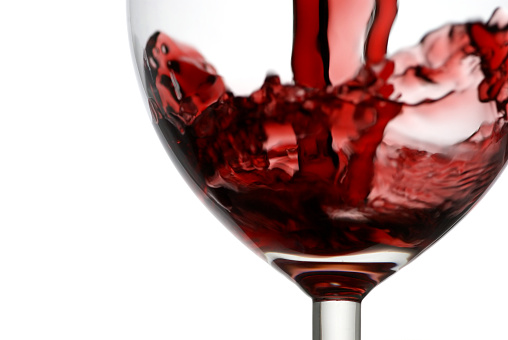 Pouring red wine into wine glass on a black background, studio shot