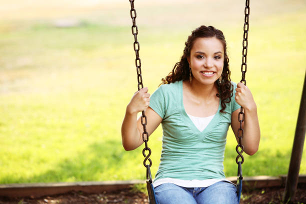A young woman sits, lost in thought, on a rustic wooden swing outdoors. Waterton, AB