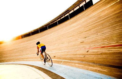A cyclist on a velodrome track riding towards the evening sun. Federaci