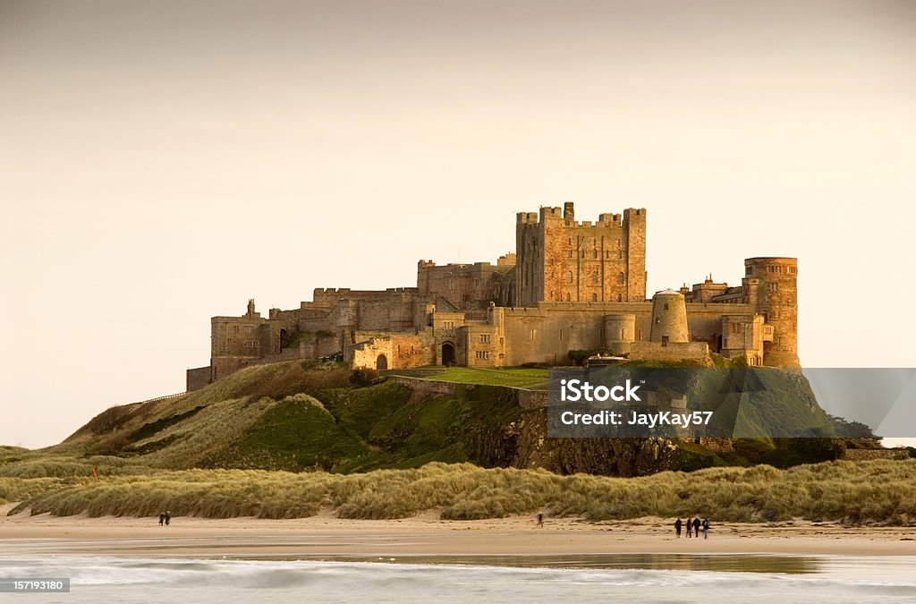 Bamburgh Castle daytime with people walking on beach Bamburgh Castle in Northumberland, England taken at dusk Castle Stock Photo