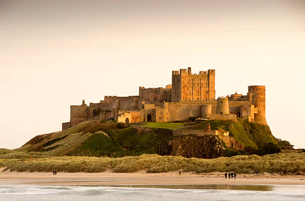 Bamburgh Castle daytime with people walking on beach Bamburgh Castle in Northumberland, England taken at dusk Bamburgh stock pictures, royalty-free photos & images