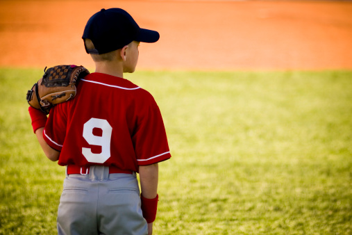 A young baseball player watches from his position in the outfield.