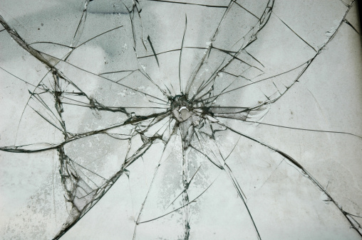 Broken glass with a hole on a blue background and with a light in the center. Texture of cracks on a broken window from explosions and gunshots