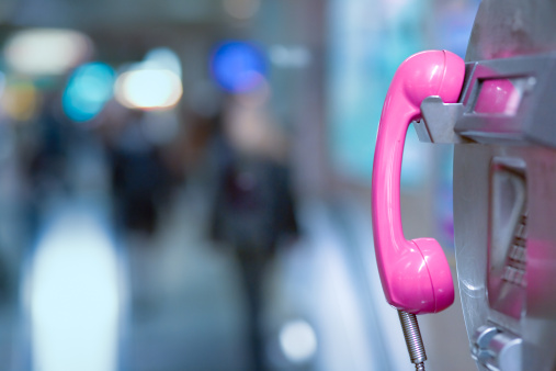 Pink handset of a public phone in front of a blurry background.