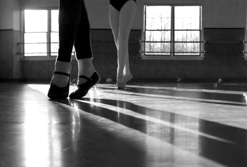 male and female ballet dancers practice in a studio. Image is black & white and back lit by window light.