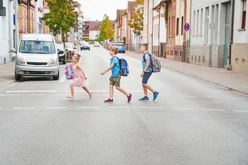 Children cross the street with rucksacks near school. Traffic rules learning at school concept. Back to school together.