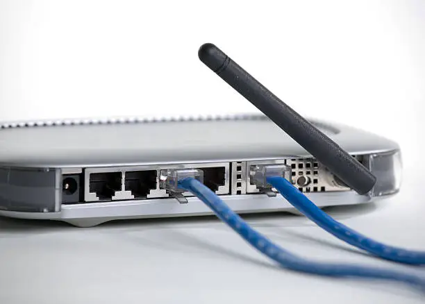 The back (ports) of a wireless router against a white background.  Two of the ports have blue network cables plugged into them.