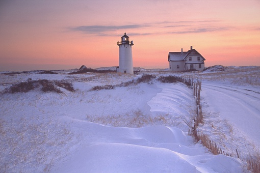 Race Point Lighthouse is located on Cape Cod where it guards the entrance to Provincetown Harbor. Surrounded by wild windswept dunes, it is accessible only by four-wheel-drive vehicle or by foot. Photo taken at sunset surrounded by snow covered dunes. Cape Cod is famous, worldwide, as a coastal vacation destination 