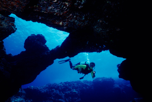 Diver swimming through blue  underwater cavern.
