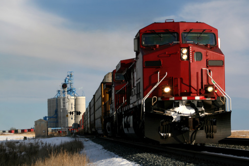 A train rumbles down the track in the prairie. Grain elevator in the background. Winter rural scene in Alberta, Canada. Railroading is a major economic industry in western Canada. This train is situated on tracks east of Calgary near Strathmore. Canadian Pacific and Canadian National are the two major companies. Additional themes here include agriculture, transportation, freight, hauling, industry, engineering, and grain. 