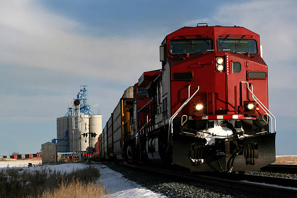 Red train on tracks in Alberta, Canada A train rumbles down the track in the prairie. Grain elevator in the background. Winter rural scene in Alberta, Canada. Railroading is a major economic industry in western Canada. This train is situated on tracks east of Calgary near Strathmore. Canadian Pacific and Canadian National are the two major companies. Additional themes here include agriculture, transportation, freight, hauling, industry, engineering, and grain.  freight train stock pictures, royalty-free photos & images